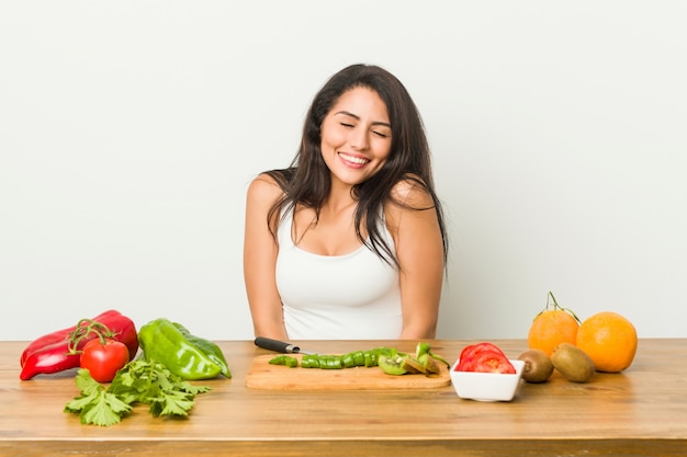 La mujer con curvas joven que prepara una comida sana ríe y cierra los ojos, se siente relajada y feliz.