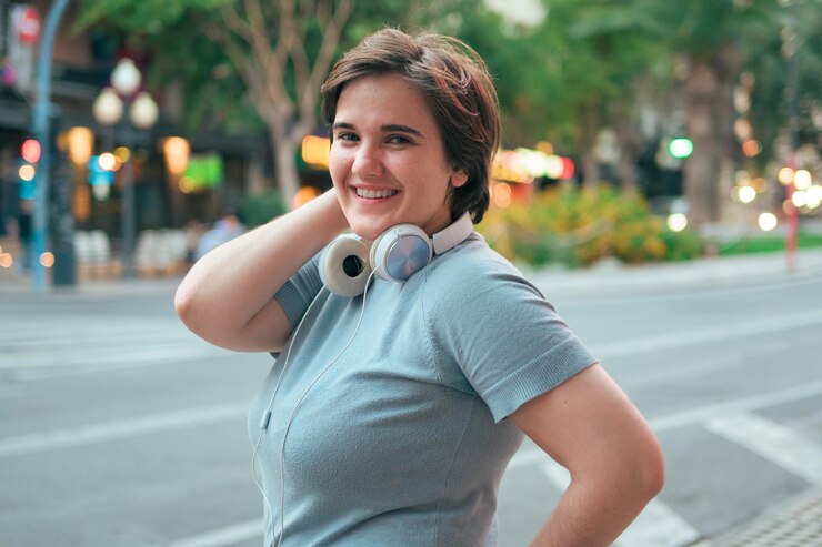 Mujer con curvas con pelo corto y auriculares mira a la cámara y sonríe en una calle de la ciudad