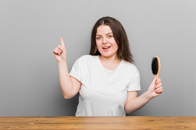 Mujer con curvas de talla grande joven sosteniendo un cepillo para el pelo