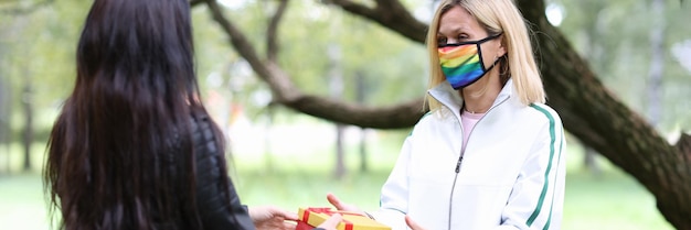 Mujer le da un regalo a un amigo con máscara con colores lgbt en el parque relación del mismo sexo entre chicas