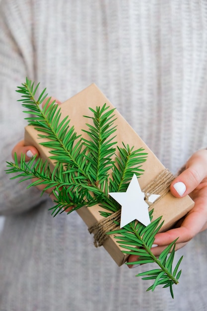 Foto mujer dando caja con regalos de año nuevo envueltos en papel artesanal y decorado con rama de abeto concepto de vacaciones y regalos hecho a mano alternativa ecológica verde regalos de navidad cero desperdicio