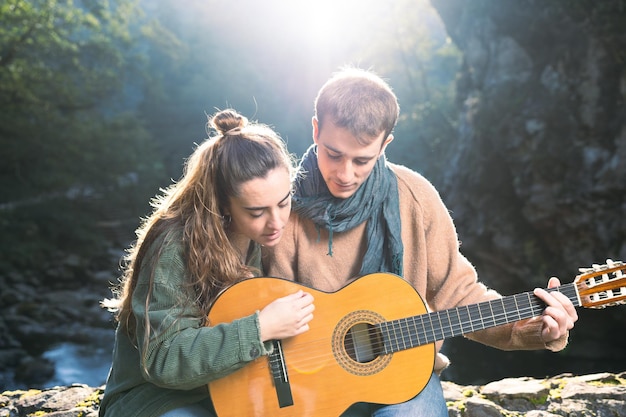 Mujer dando una lección de guitarra a un joven al aire libre