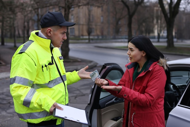 Foto mujer dando soborno al oficial de policía cerca del coche al aire libre