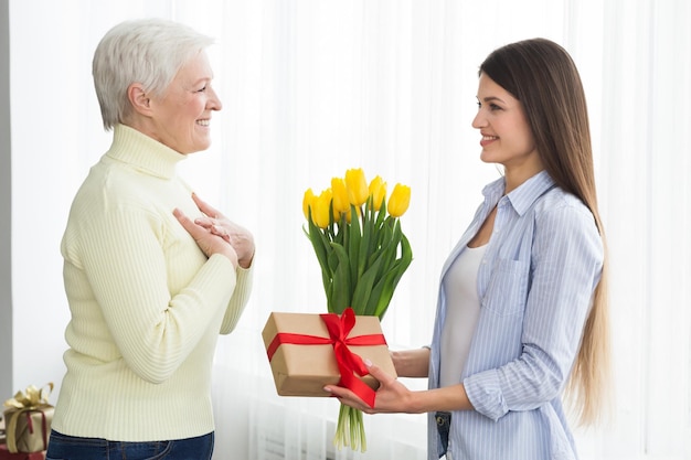 Mujer dando tulipanes y caja de regalo a su madre madura