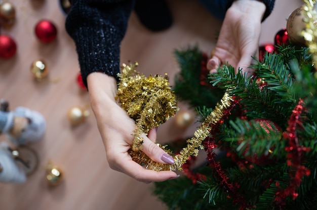 Mujer decorando el árbol de navidad de vacaciones con cinta dorada