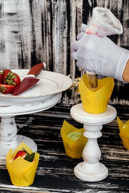 Mujer decorando sabrosos pastelitos de fresa.