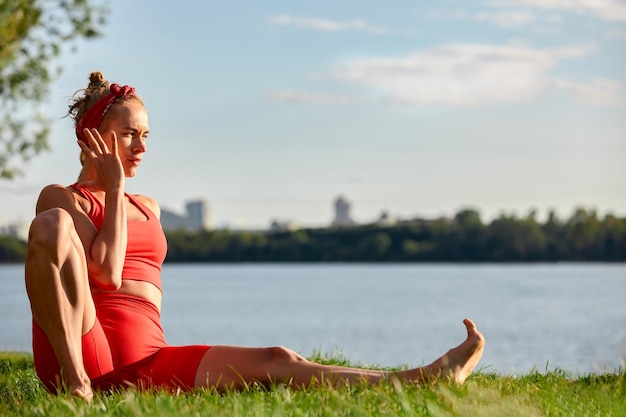 Una mujer se dedica a la gimnasia de flujo animal al aire libre cerca del río sobre hierba verde con ropa roja