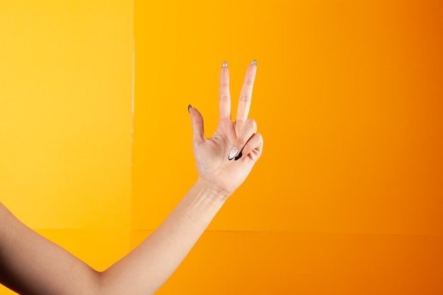 Mujer con dedos muestra tres sobre fondo naranja