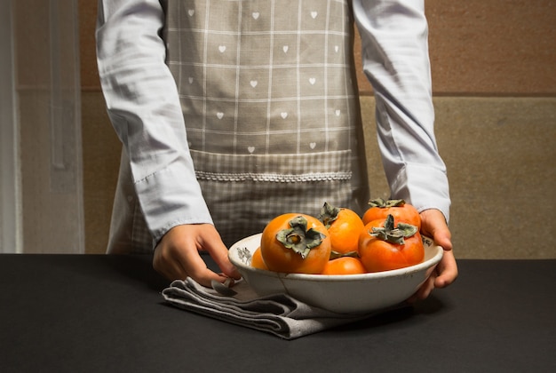 Foto mujer en delantal de cocina con plato de caqui