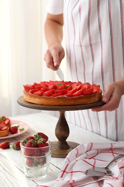 Mujer en delantal cortó la tarta de fresa.