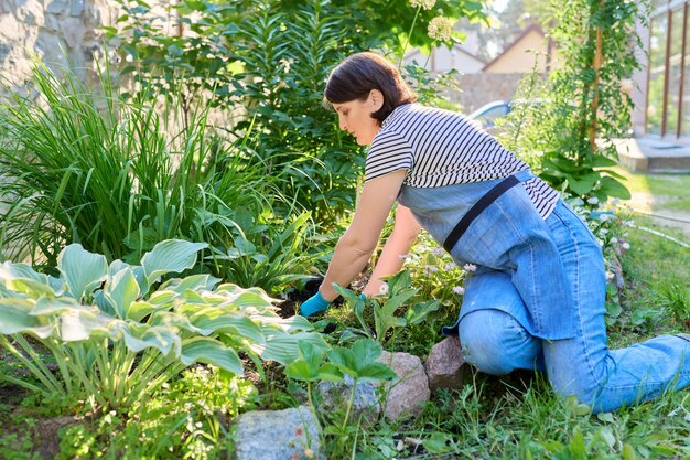 Mujer en un delantal de guantes de jardinería con una pala plantando plantas con flores