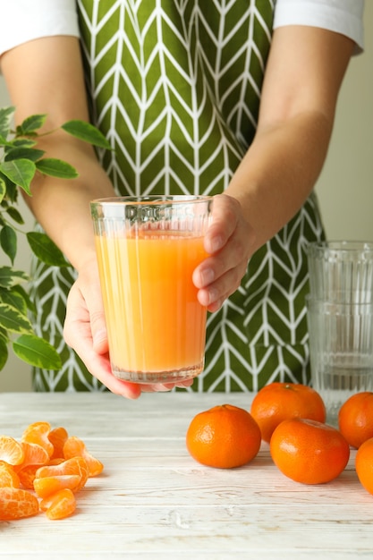 Mujer en delantal tiene vaso con jugo de mandarina