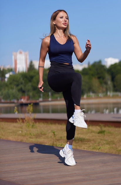 Mujer delgada atlética en un día soleado corre a lo largo del terraplén o parque