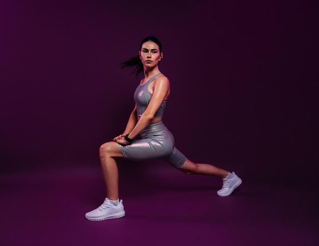 Mujer delgada con atuendo deportivo plateado calentando su cuerpo sobre un fondo magenta