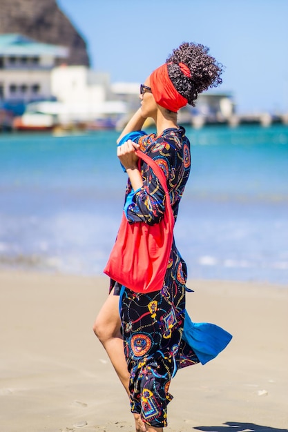 Mujer delgada de belleza latina posando y caminando con ropa colorida de verano en una playa ventosa tropical