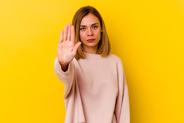 Mujer delgada caucásica joven aislada en amarillo que se coloca con la mano extendida que muestra la señal de stop, previniéndole.