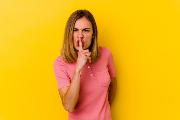 Mujer delgada caucásica joven aislada en la pared amarilla que guarda un secreto o que pide silencio.