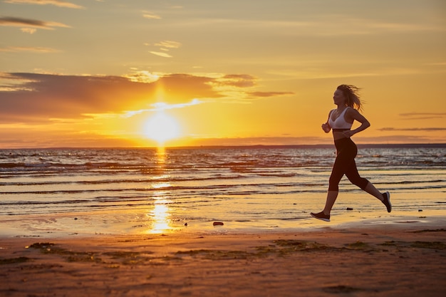 Mujer delgada corre en la orilla durante la puesta de sol