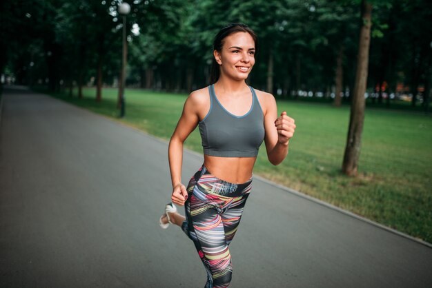 Mujer delgada para correr en la acera en el parque de verano. Corredoras en el entrenamiento de la mañana al aire libre