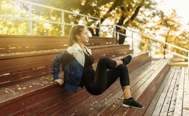 Una mujer delgada en forma practica flexiones inversas para las manos desde soportes de madera. Entrenamiento al aire libre