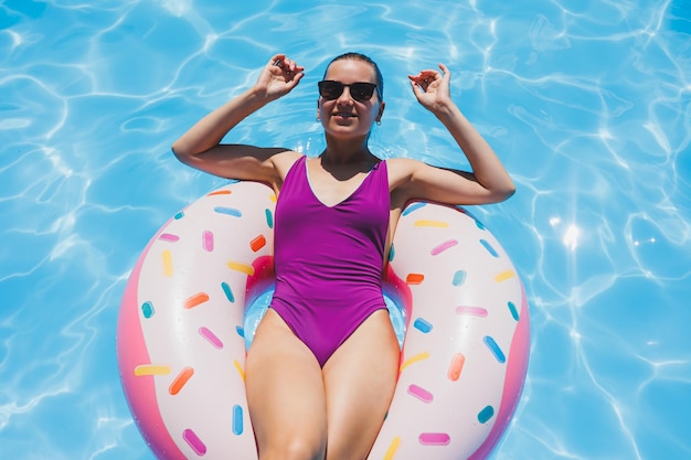 Mujer delgada con gafas de sol en la piscina en un anillo de natación inflable en un traje de baño brillante foto de verano fotografía de natación fotos de mujer de verano Moda de playa