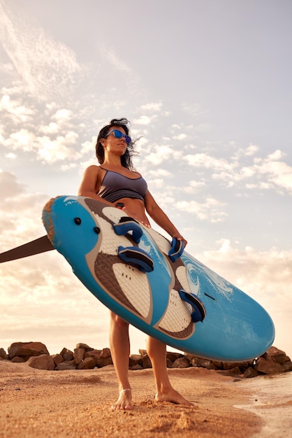 Foto mujer delgada joven lleva una tabla de surf en la playa