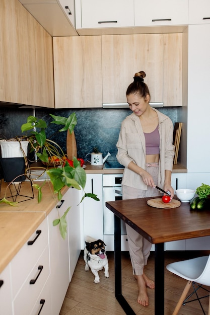 Mujer delgada joven con peinado de moño cocina verduras en la cocina en estilo interior escandinavo