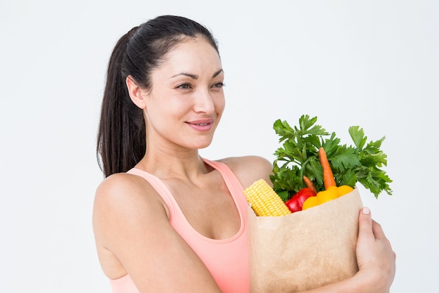 Mujer delgada que sostiene el bolso con alimentos saludables sobre fondo blanco