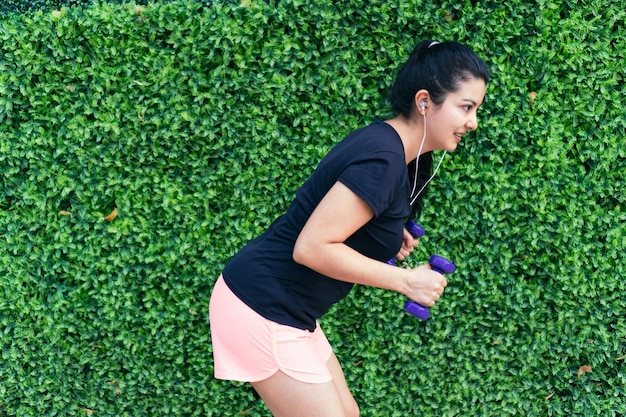 Mujer delgada en ropa deportiva haciendo ejercicio con pesas en el parque por la mañana antes de la dura jornada de trabajo