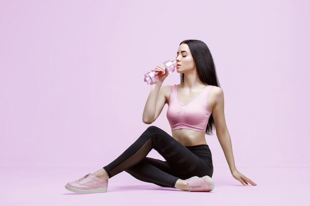 Mujer delgada en ropa deportiva moderna bebiendo agua de la botella para mantenerse hidratada después del entrenamiento