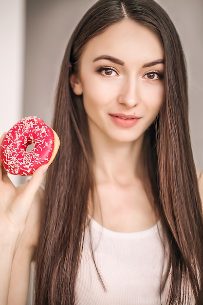 Mujer delgada sostenga en la mano rosquilla rosa