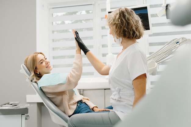 Mujer dentista en consultorio dental hablando con paciente femenino y preparándose para el tratamiento