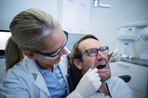 Mujer dentista examinar paciente masculino con herramientas