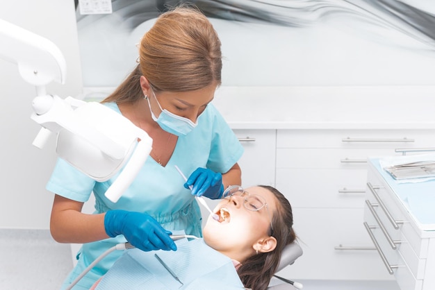 Mujer dentista con guantes está trabajando en la boca de una mujer joven