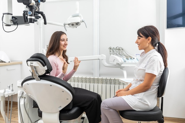 Mujer dentista hablando con un paciente joven durante una cita en una clínica dental moderna antes del tratamiento dental