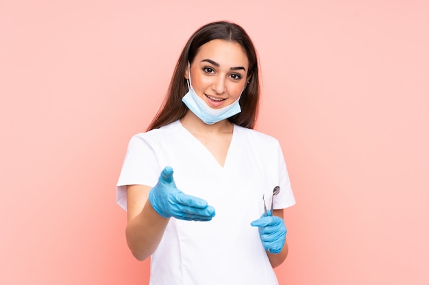 Mujer dentista con herramientas aisladas en apretón de manos de pared rosa después de buen trato
