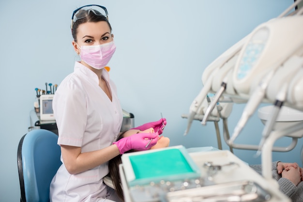 Mujer dentista con herramientas dentales - espejo y sonda para tratar los dientes del paciente y mirando a la cámara en la oficina de la clínica dental.