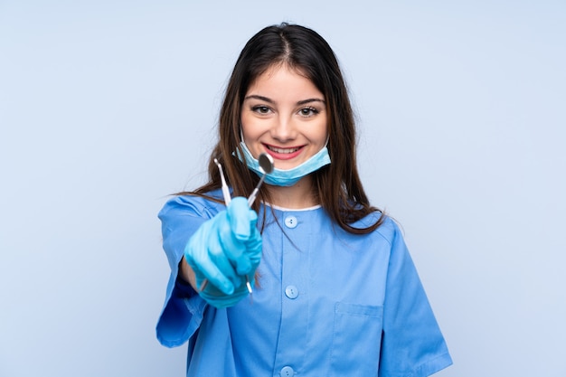 Mujer dentista con herramientas sobre pared azul aislada