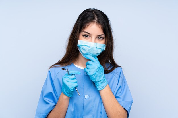 Mujer dentista con herramientas sobre pared azul aislada