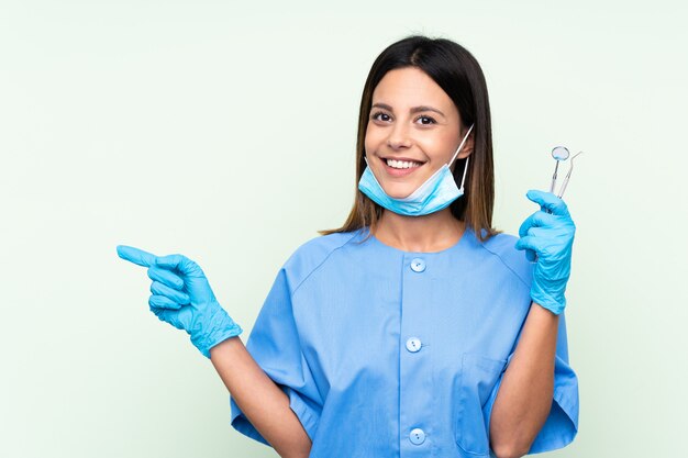 Mujer dentista con herramientas sobre la pared verde que señala el dedo hacia un lado
