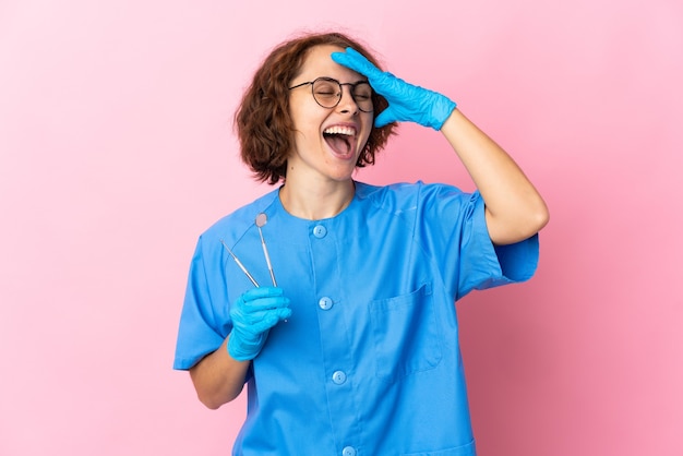 Mujer dentista inglés sosteniendo herramientas sobre aislado en pared rosa sonriendo mucho