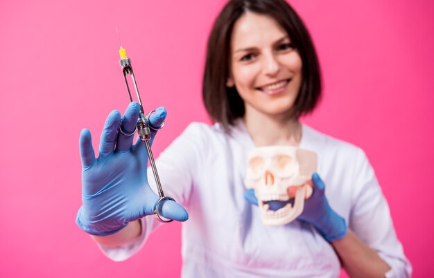 Mujer dentista con una jeringa de carpool inyecta anestésico en la encía del cráneo artificial