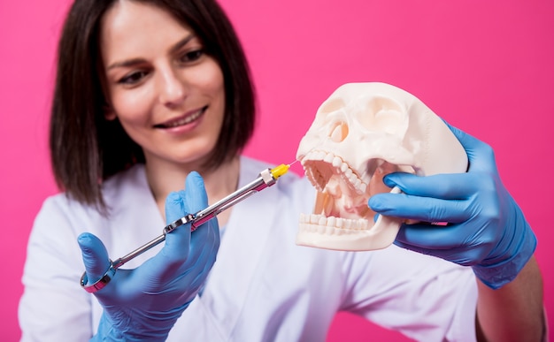 Mujer dentista con una jeringa de carpool inyecta anestésico en la encía del cráneo artificial