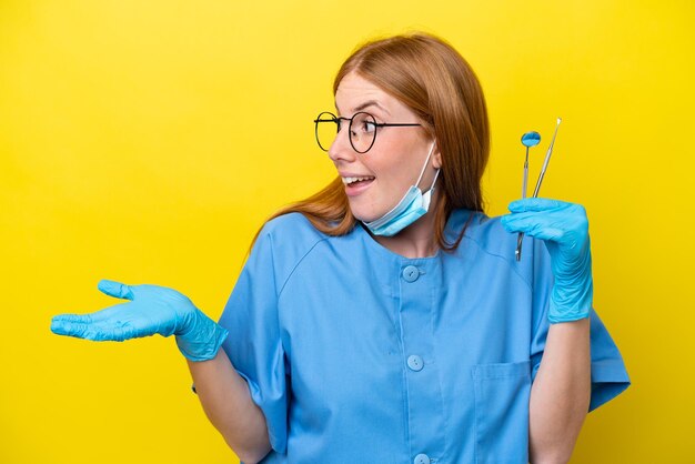 Mujer dentista joven pelirroja aislada de fondo amarillo con expresión de sorpresa mientras mira de lado