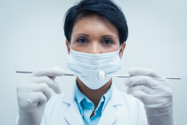 Mujer dentista en máscara quirúrgica sosteniendo herramientas dentales