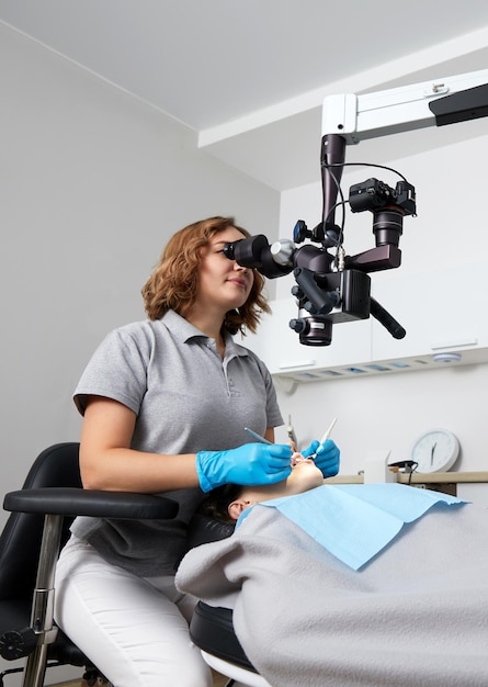 Mujer dentista con microscopio que trata los dientes del paciente en la oficina de la clínica dental Medicina odontología y concepto de atención médica