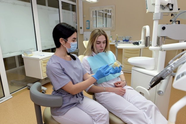 Mujer dentista mostrando un modelo de mandíbula artificial a un paciente