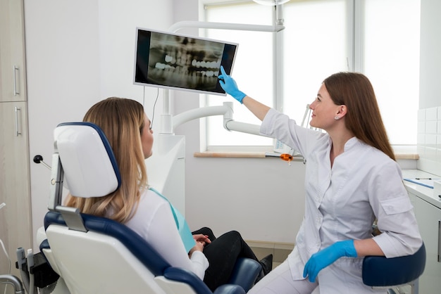 Foto mujer dentista mostrando radiografía de dientes al paciente en la clínica