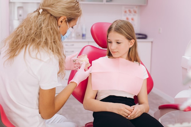 Mujer dentista muestra un modelo de dientes a una adolescente en una clínica dental