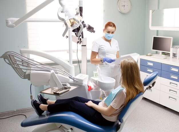 Mujer dentista con paciente niña hablando en la oficina de la clínica dental